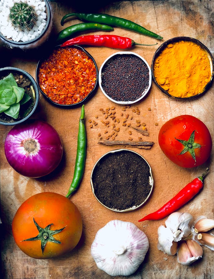 A vibrant flat lay of various spices and vegetables on a wooden countertop showcasing culinary diversity.