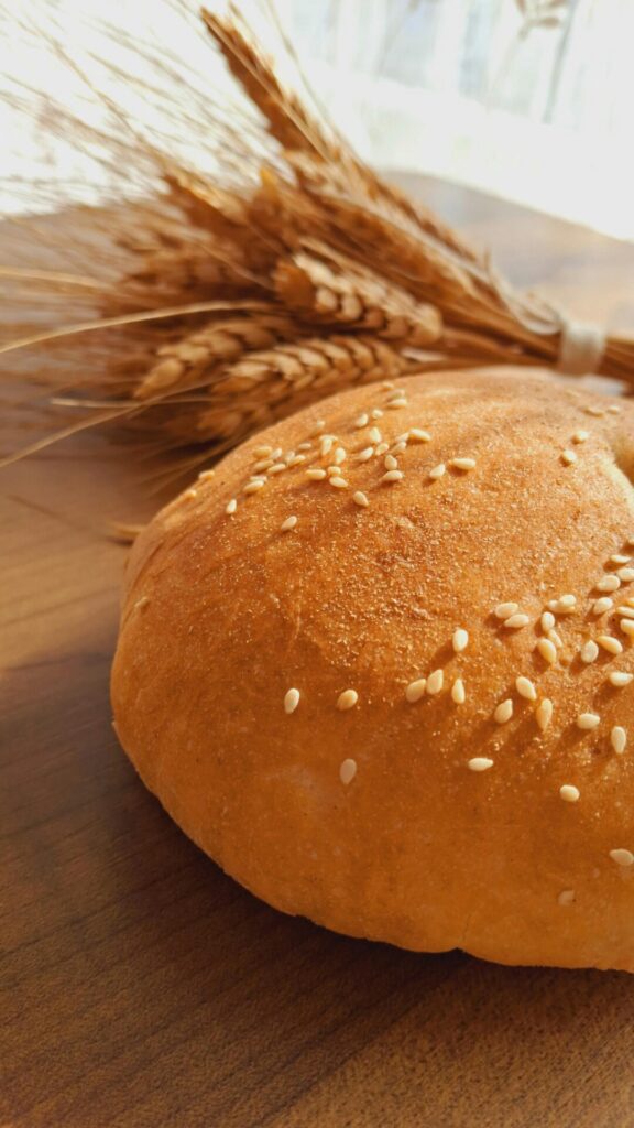 Close-up of fresh sesame seed bread with wheat stalks on a wooden table.